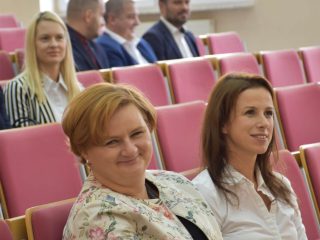 Dwie uśmiechnięte uczestniczki uroczystości nagród siedzą obok siebie w auli.