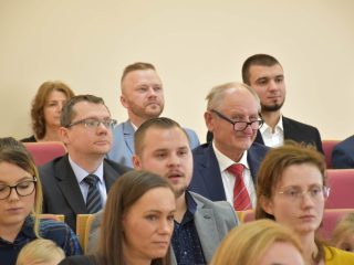 Uczestnicy uroczystości wręczenia nagród siedzą w rzędach czerwonych foteli.