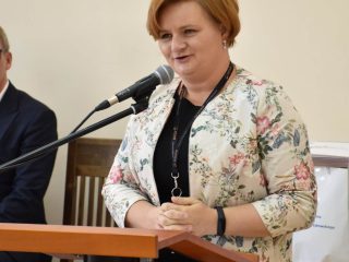 Kobieta w kwiecistej marynarce przemawia przy mównicy.