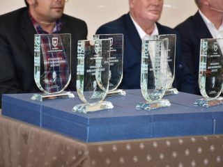 Szklane statuetki ustawione na niebieskich pudełkach przed uczestnikami uroczystości.