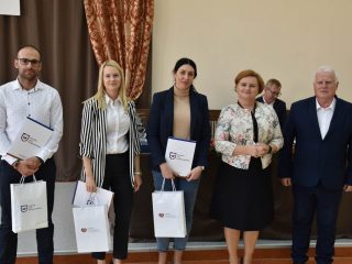 Troje nagrodzonych z dyplomami i białymi torbami pozuje obok organizatorów uroczystości.