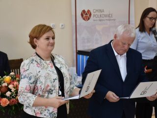 Kobieta w kwiecistej marynarce i siwowłosy mężczyzna stoją z otwartymi teczkami.