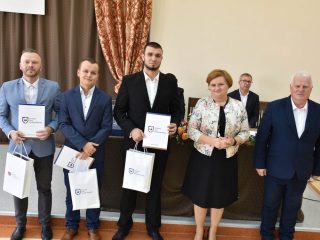 Trzej nagrodzeni mężczyźni pozują z dyplomami i torbami obok kobiety i siwowłosego mężczyzny.
