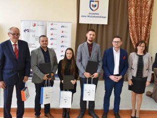 Wyróżnieni uczestnicy i organizatorzy pozują do zdjęcia z dyplomami oraz torbami.