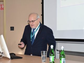 Prelegent z pilotem prezentacyjnym omawia slajd przy mównicy.