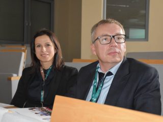 Dwoje uczestników konferencji z identyfikatorami siedzi w sali wykładowej.