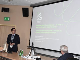Prelegent w ciemnym garniturze przedstawia prezentację przy mównicy podczas konferencji naukowej.