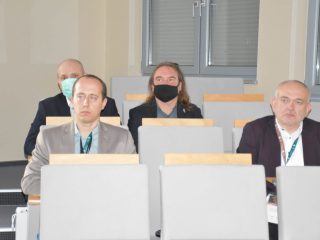 Uczestnicy konferencji siedzą w rzędach foteli; część ma maseczki.