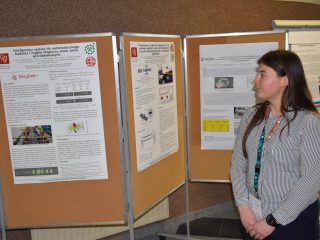 Uczestniczka konferencji w pasiastej bluzce stoi obok posterów naukowych.