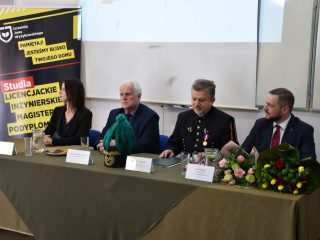 Kobieta i trzej mężczyźni siedzą przy stole z kwiatami i czakiem górniczym z zielonym pióropuszem.
