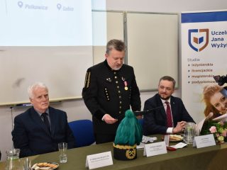Mężczyzna w mundurze górniczym przemawia przy stole, przy którym siedzą uczestnicy uroczystości.