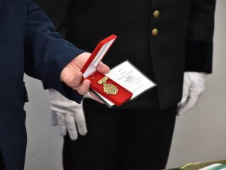 Zbliżenie na odznaczenie w otwartym czerwonym etui trzymanym przez uczestnika uroczystości.