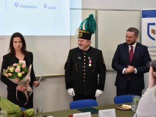 Kobieta z bukietem i dokumentem pozuje z dwoma mężczyznami podczas uroczystości odznaczeń CBJ.