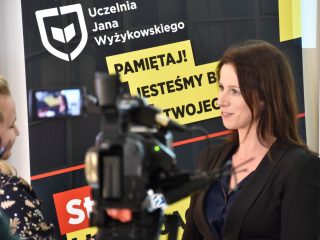 Kamera rejestruje wywiad z kobietą na tle banera Uczelni Jana Wyżykowskiego.
