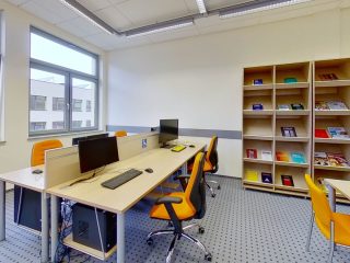 Stanowiska komputerowe obok regału z książkami w pomieszczeniu UJW.