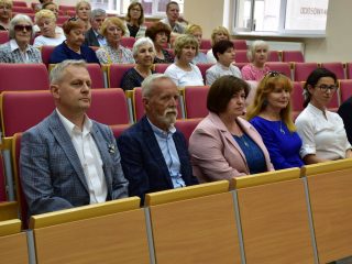 Słuchacze i goście zakończenia roku PUTW siedzą w czerwonych fotelach auli.