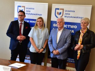 Czworo uczestników podpisania porozumienia ze szkołą pozuje przy stole.
