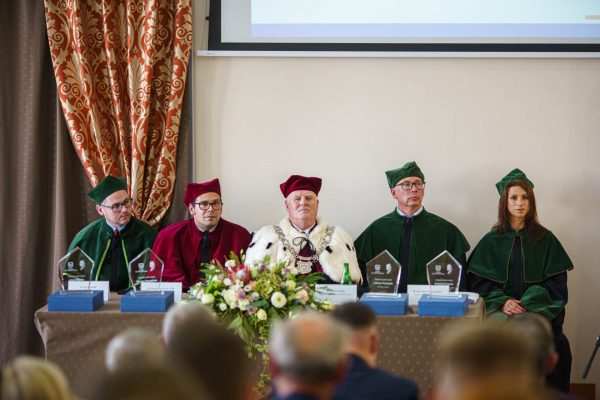 Władze uczelni w togach przy stole prezydialnym podczas inauguracji roku akademickiego 2022/2023.