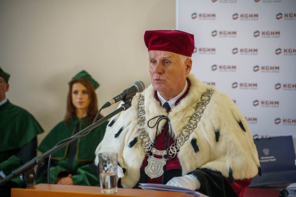 Mężczyzna w stroju rektorskim przemawia przy mikrofonie podczas inauguracji roku akademickiego.