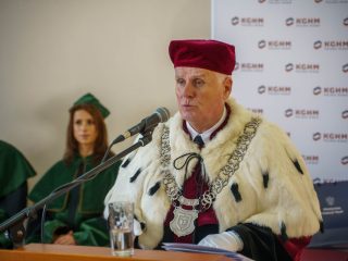 Mężczyzna w stroju rektorskim przemawia przy mikrofonie podczas inauguracji roku akademickiego.