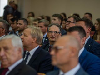 Uczestnicy inauguracji roku akademickiego siedzą w rzędach foteli w auli.