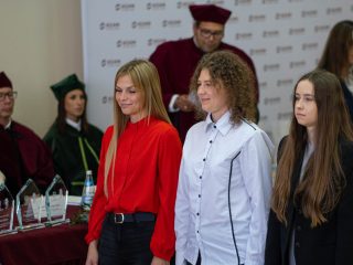 Troje studentów stoi przed stołem prezydialnym podczas uroczystości.