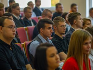 Studenci i goście słuchają wystąpienia, siedząc w rzędach foteli.