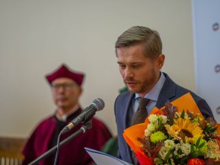 Mężczyzna z bukietem kwiatów odczytuje tekst do mikrofonu.