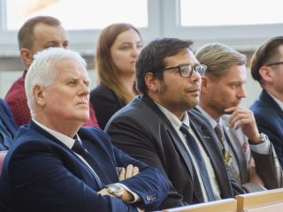 Mężczyźni w garniturach siedzą wśród publiczności uroczystości wręczenia nagród.