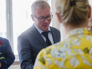 Mężczyzna w szarym garniturze i okularach uczestniczy we wręczaniu nagród.