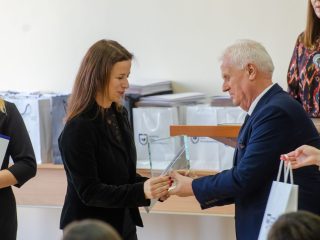 Kobieta w czarnym stroju odbiera szklaną statuetkę z rąk przedstawiciela uczelni.