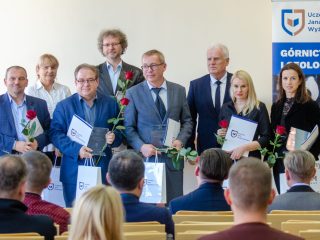 Wyróżnieni uczestnicy pozują z dyplomami, czerwonymi różami i torbami upominkowymi.