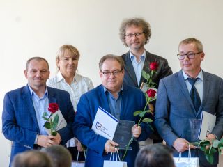 Grupa nagrodzonych pozuje z różami i statuetkami obok organizatorów.