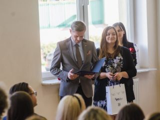 Kobieta z czerwoną różą i torbą upominkową stoi obok mężczyzny przeglądającego dokument.