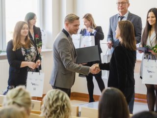Mężczyzna w szarym garniturze gratuluje kobiecie podczas wręczania nagród.