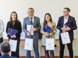 Pięcioro nagrodzonych pozuje z fioletowymi teczkami, różami i torbami upominkowymi.