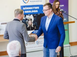 Mężczyzna w okularach i niebieskiej marynarce ściska dłoń organizatora.