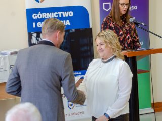 Kobieta w białej bluzce odbiera gratulacje od organizatora uroczystości.