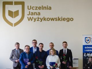 Grupa nagrodzonych pozuje z organizatorem pod napisem Uczelnia Jana Wyżykowskiego.