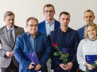 Nagrodzeni z fioletowymi teczkami i czerwonymi różami pozują do zdjęcia.