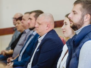 Uczestnicy wręczenia nagród siedzą w rzędzie foteli, widoczni z boku.