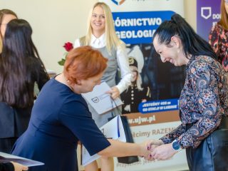 Organizatorka w granatowej sukience ściska dłonie kobiety we wzorzystej bluzce.