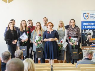 Grupa wyróżnionych osób z różami, dyplomami i upominkami pozuje obok organizatorki.