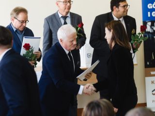 Siwowłosy przedstawiciel uczelni gratuluje kobiecie w czarnym stroju.