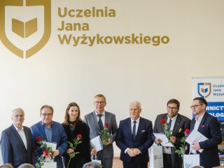 Nagrodzeni pozują z dyplomami i czerwonymi różami pod logo UJW.