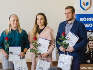 Dwie kobiety i mężczyzna pozują z dyplomami, czerwonymi różami oraz torbami upominkowymi.