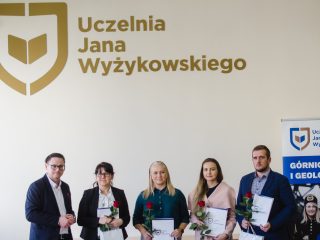Pięcioro uczestników wręczenia nagród pozuje pod logo Uczelni Jana Wyżykowskiego.