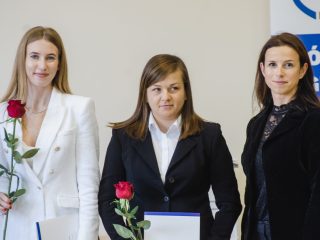 Dwie wyróżnione kobiety z różami i dyplomami pozują obok kobiety w czarnym stroju.
