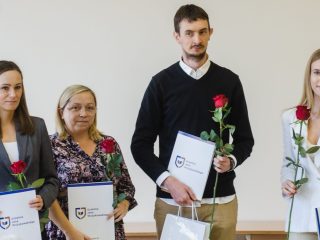 Troje kobiet i mężczyzna prezentują dyplomy oraz czerwone róże.