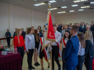 Studenci stoją wokół sztandaru uczelni podczas uroczystości ślubowania.